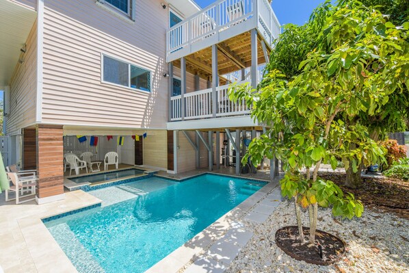A two-story building with a swimming pool, outdoor seating, and a tree. - Gulf View Retreat! Pool, Decks and 2 King Beds! (Anna Maria)