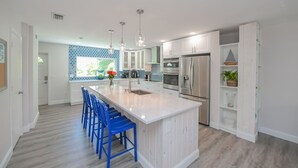 Een moderne keuken met een groot eiland, witte kasten en blauwe stoelen.