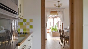 Eine Küche mit Holzausstattung, ein Essbereich mit Korbmöbeln und Blick durch eine Tür in einen Wohnraum.