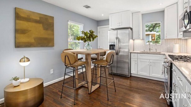 Una cocina moderna con armarios blancos, un refrigerador de acero inoxidable y un comedor con una mesa redonda y sillas.