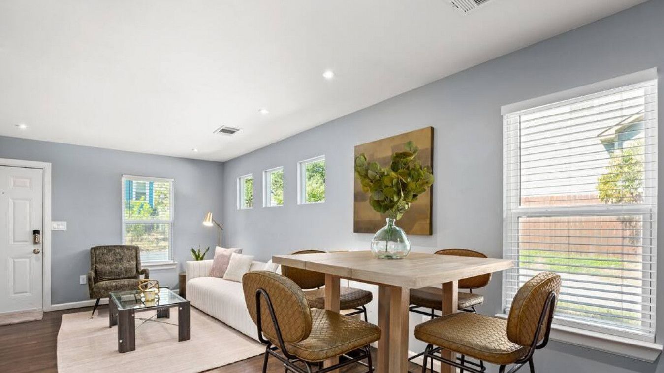 A modern living room with a dining area, featuring a wooden table, wicker chairs, a sofa, and a coffee table.