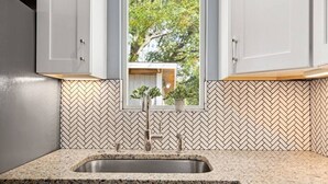 Una cocina con salpicadero de azulejos en espiga, encimera de granito y ventana sobre el fregadero.
