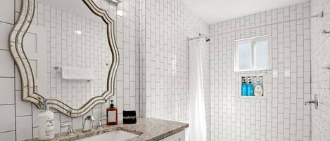 A bathroom with a white tiled wall, a large mirror, a granite countertop, a sink, a toilet, and a shower curtain.