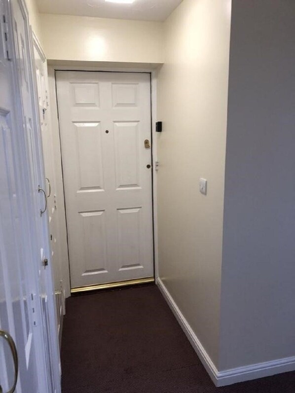 A hallway with a white door, a light switch, and a thermostat on the wall. - Glass Green Apartment, Northallerton (Northallerton)