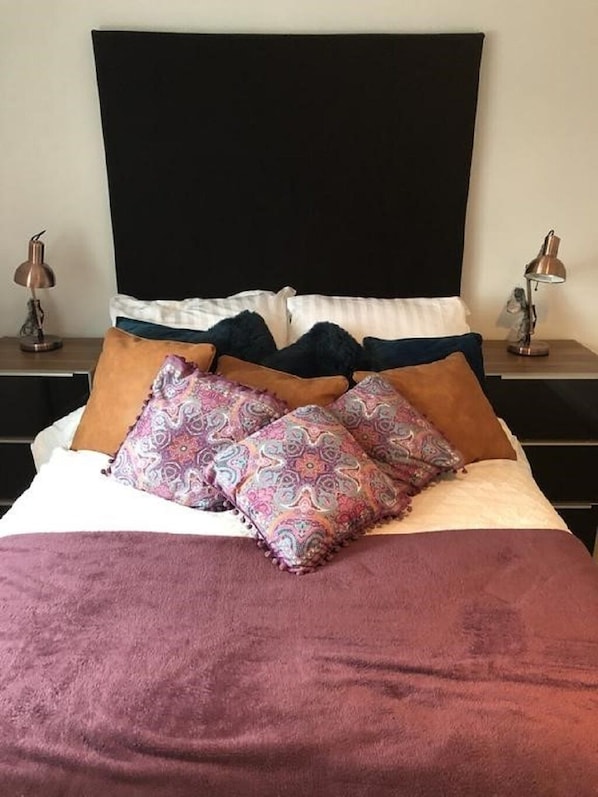 Een bed met een zwart hoofdeinde, meerdere kussens en twee bedlampen.