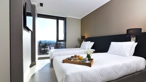 Habitación de hotel con dos camas, un ventanal grande y una bandeja de desayuno sobre la cama.