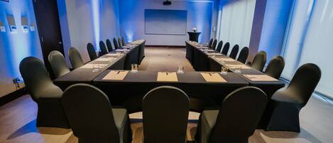 Un salón de conferencias con una larga mesa, sillas negras y una pantalla para proyector.