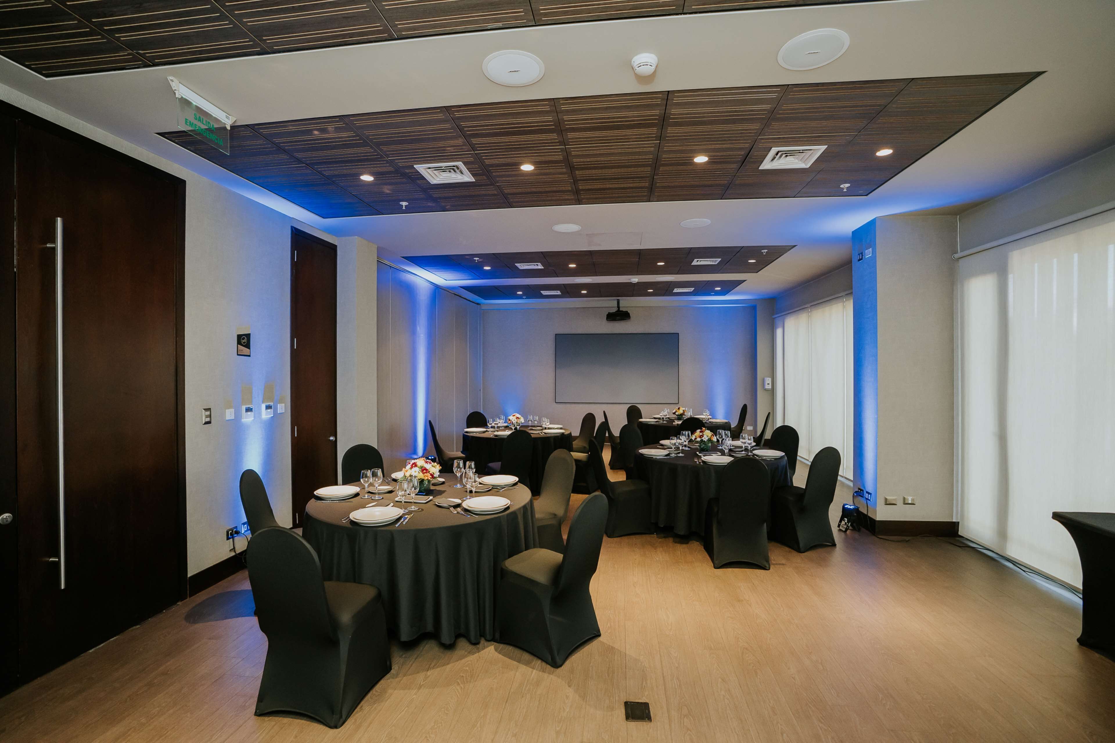A conference room with round tables, black chairs, and a projector screen.