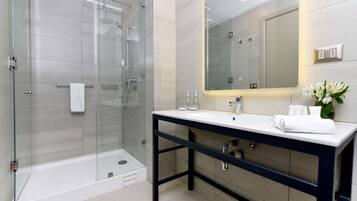 Un baño moderno con ducha de vidrio, lavamanos blanco sobre encimera oscura y un espejo grande por encima.