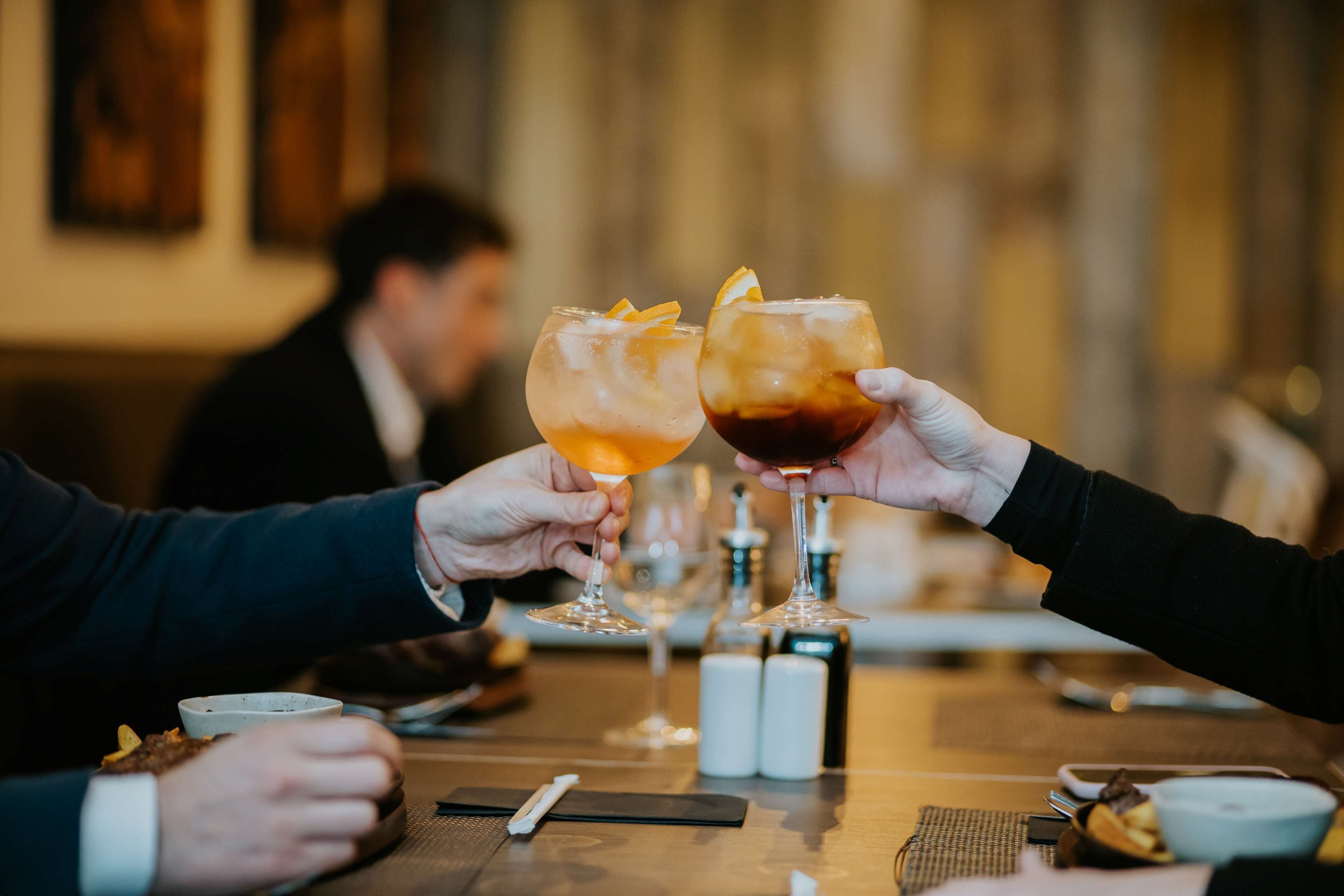Deux personnes trinquent avec leurs boissons autour d’une table dans un restaurant.