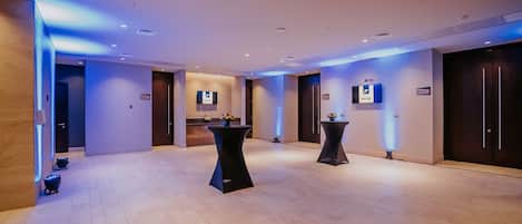 A spacious hotel lobby with a modern design, featuring a reception desk, two side tables with floral centerpieces, and a large mirror on the wall.