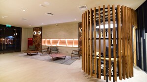 Un vestíbulo moderno con un separador de madera, zona de estar con sillas y una pared con un elemento decorativo luminoso geométrico.