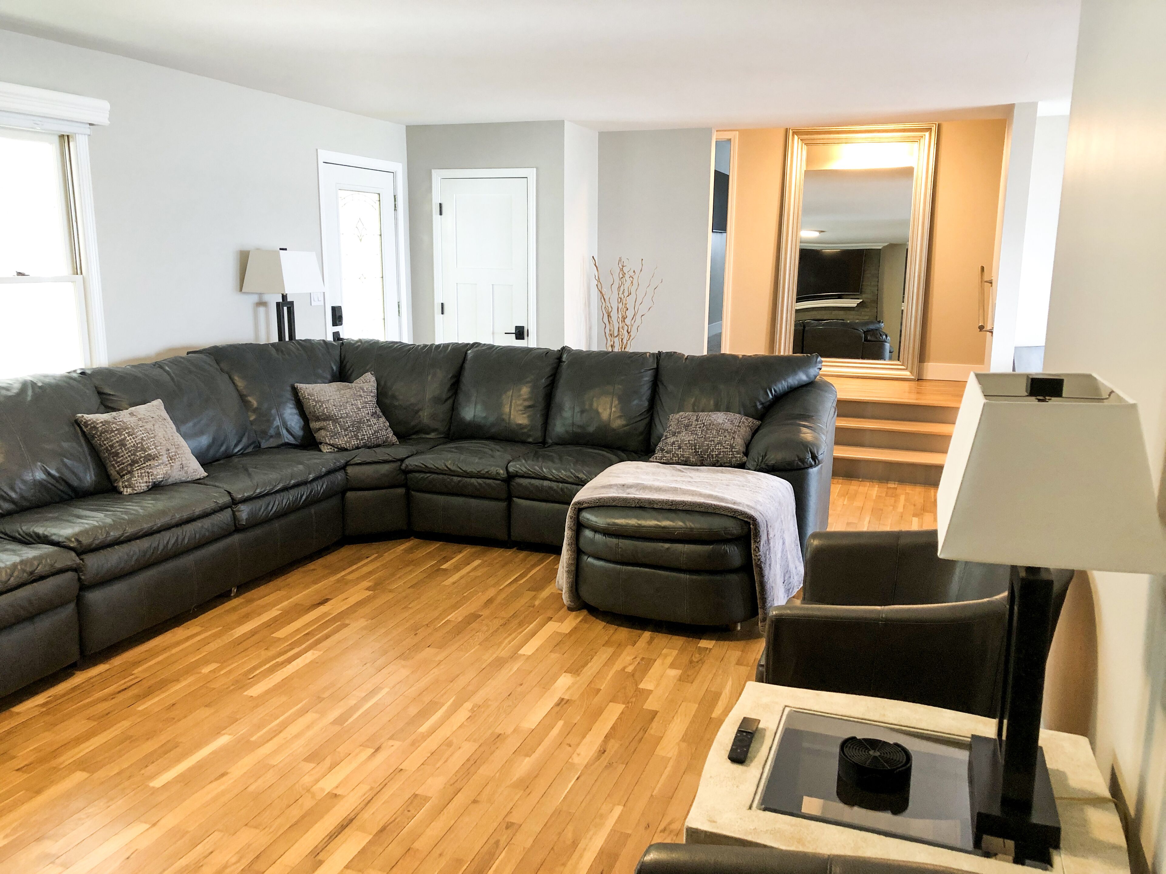 A modern living room with a sectional sofa, a small ottoman, a glass coffee table, and a floor lamp.