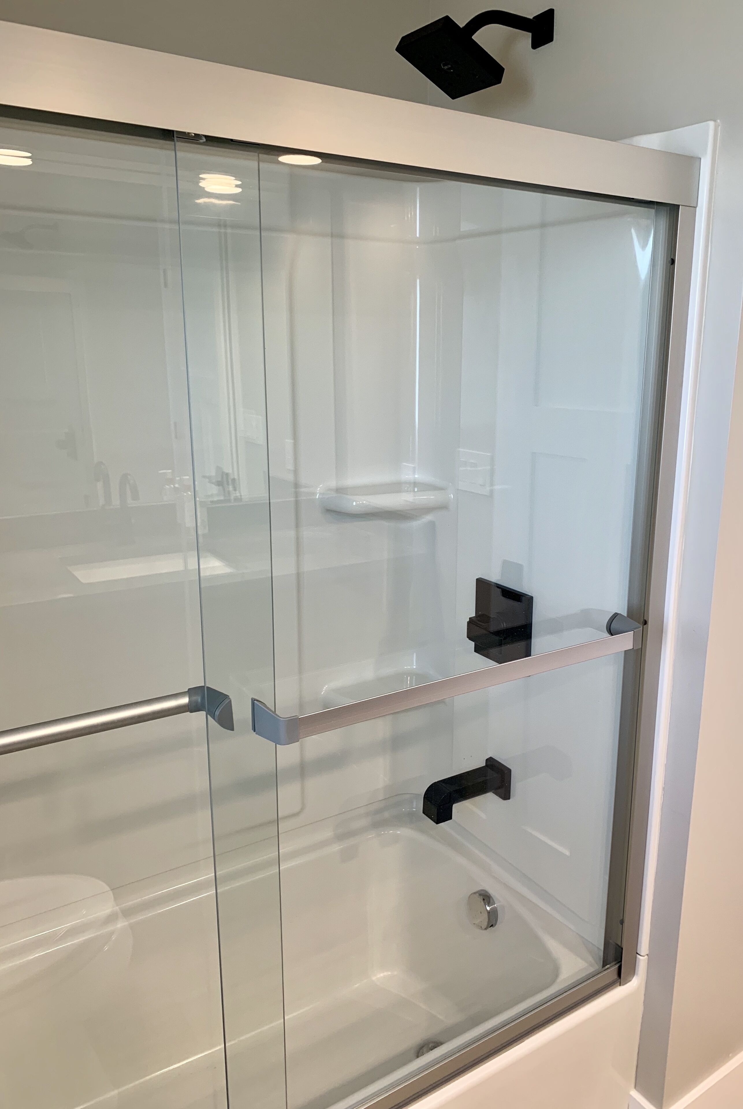 A glass-enclosed shower with a faucet and a shelf.