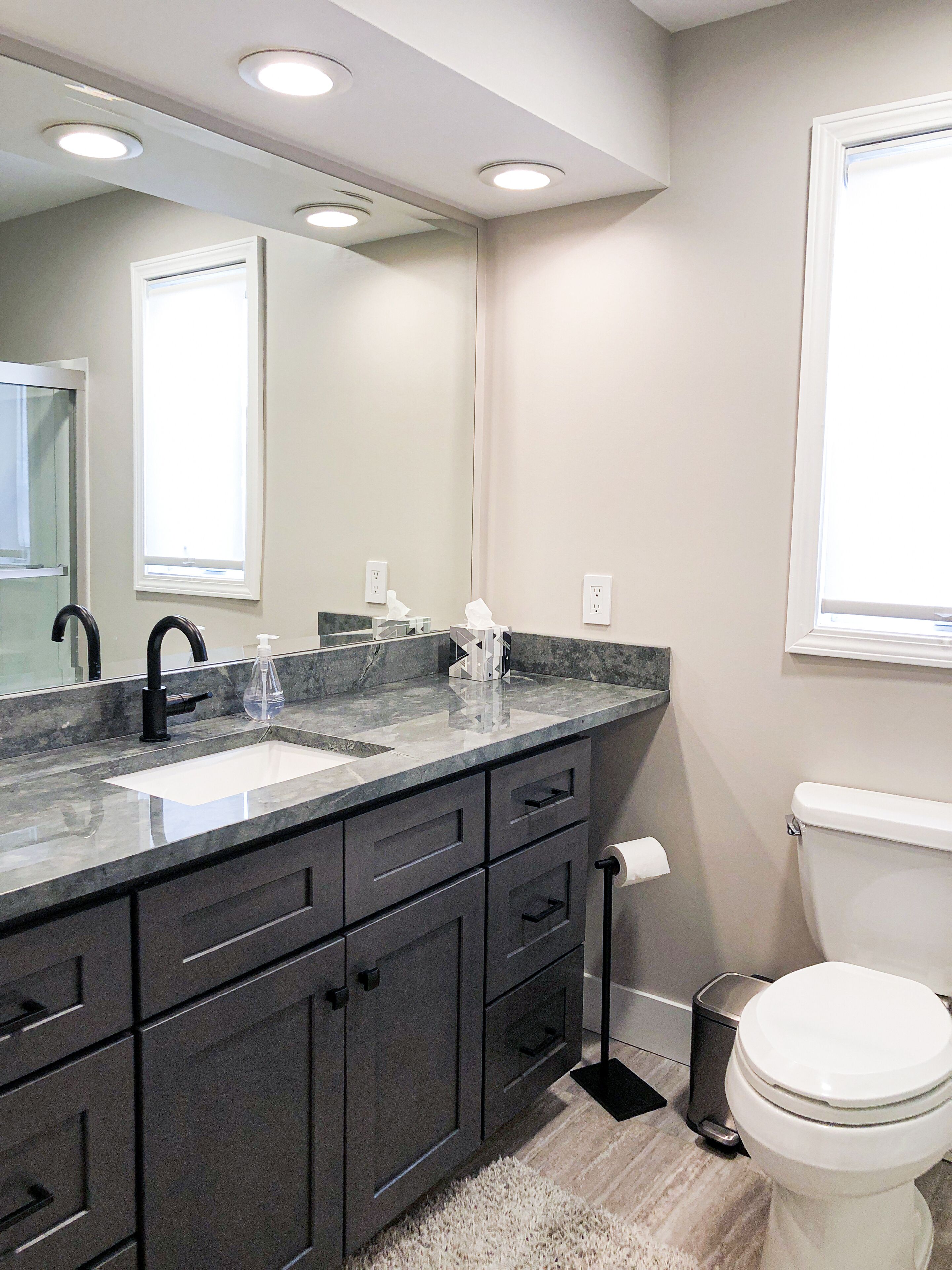 A modern bathroom with a large mirror, dark cabinetry, a white sink, and a toilet.