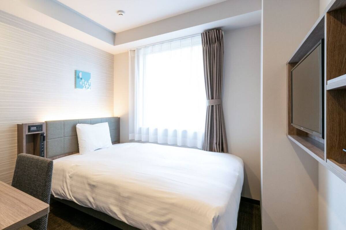 A hotel room with a bed, a desk, a chair, a television, and a window with curtains.