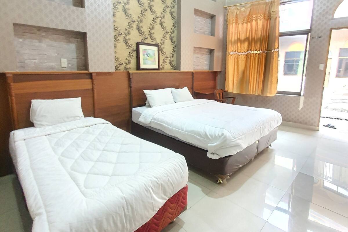 A hotel room with two beds, a patterned wallpaper, a framed picture, and a window with curtains.