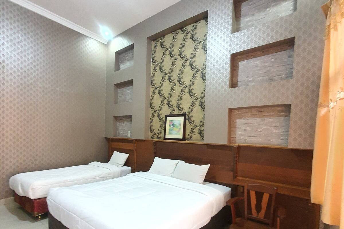 A hotel room with two beds, a wooden headboard, a small wooden chair, and a patterned wallpaper on the wall.