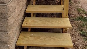 A wooden outdoor staircase leading up to a building with a stone facade.