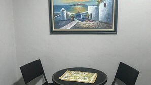 A room with a round table and two chairs, a framed painting on the wall, and a window with a view of the sea.