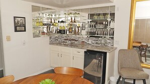 A compact kitchen with a dining area, featuring a built-in dishwasher, a wooden dining table, and a chair.