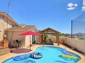 A backyard with a swimming pool, inflatable toys, a gazebo, and outdoor furniture.