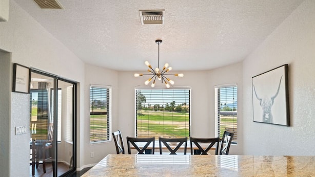 A dining area with a granite table, chairs, a chandelier, and large windows with a view of a golf course.