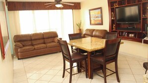 A living room with a brown leather sofa, a dining table with chairs, a ceiling fan, a flat-screen TV, and a bookshelf. - My little paradise on earth.  (Chicxulub, Progreso, Yucatán)