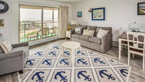 A living room with a sofa, armchair, round coffee table, and a rug with anchor patterns. - Gearhart House G662 (Gearhart)
