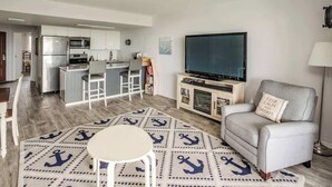 A modern living room with a TV, a sofa, and a dining area with a kitchen in the background. - Gearhart House G662 (Gearhart)