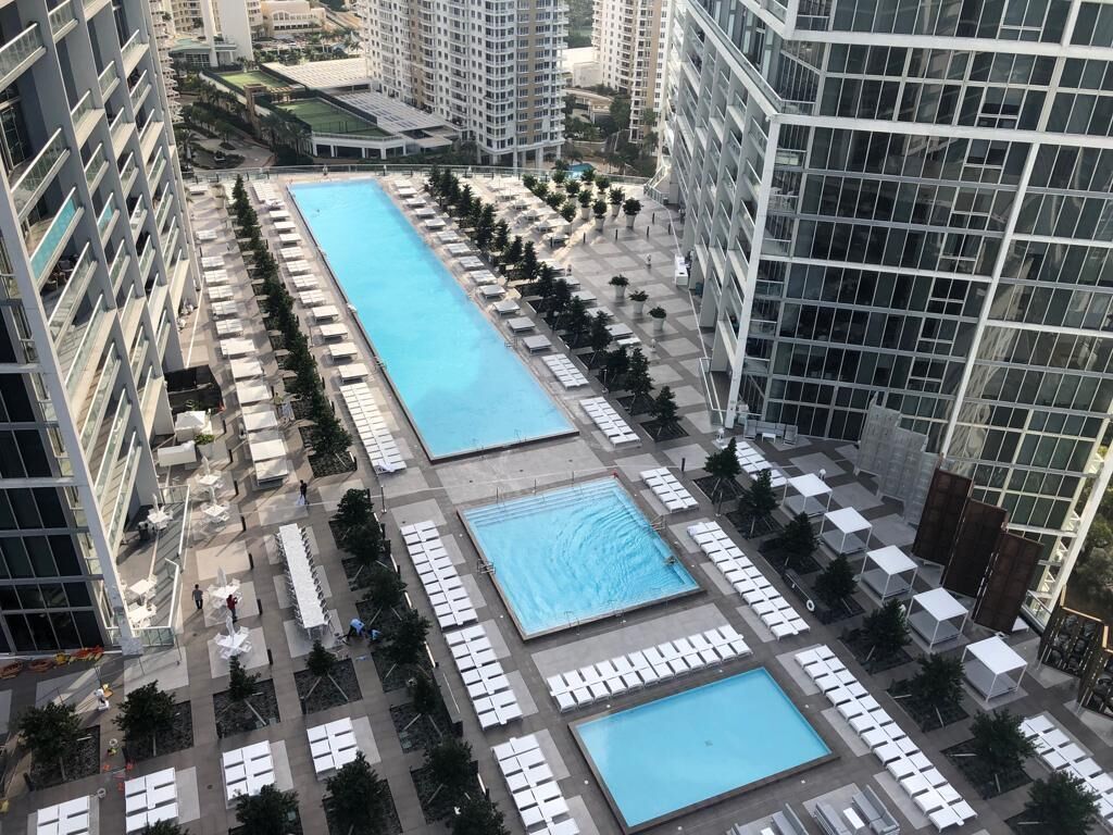 A high-rise building with a rooftop pool area, multiple swimming pools, and sun loungers.