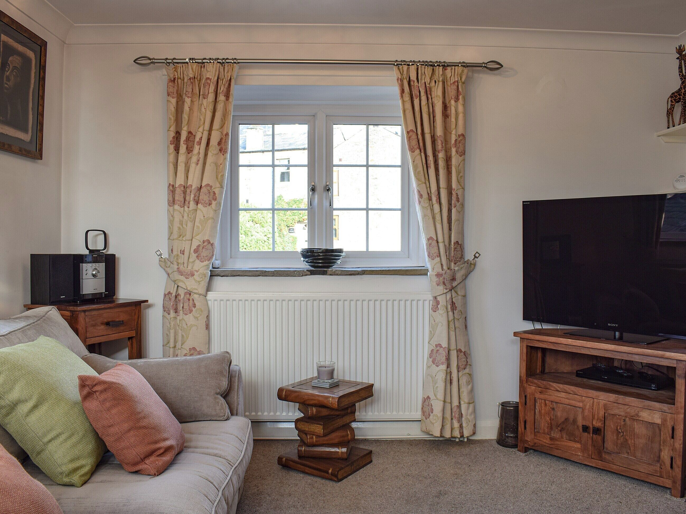 A living room with a sofa, a television, a small table with a candle, and a window with curtains.