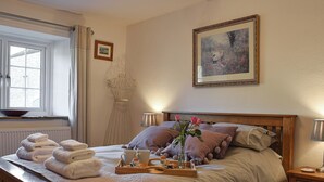 A neatly made bed with a floral pillow arrangement, a bedside table with a lamp, and a window with a view of the outside. - 3 bedroom accommodation in Giggleswick, near Settle (Giggleswick, near Settle)