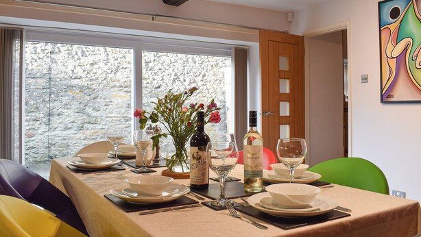 A dining table set for four with wine bottles, glasses, and a vase of flowers. - 3 bedroom accommodation in Giggleswick, near Settle (Giggleswick, near Settle)