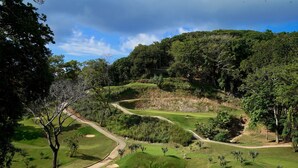 A golf course with a winding path, sand bunkers, and lush greenery. - West Bay Golf Club & Villas (Roatan)