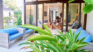 A modern living area with wicker furniture, a glass door leading to a dining area, and a view of the outdoors. - West Bay Golf Club & Villas (Roatan)