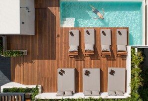 A rooftop pool area with wooden flooring, lounge chairs, and a person swimming.