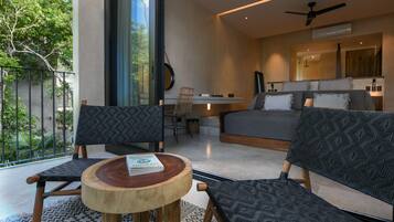 A modern hotel room with a large bed, two patterned chairs, a small wooden table, a desk, and a balcony with a view of greenery.