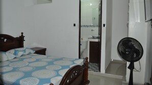 A bedroom with a bed, a bedside table, a mirror, a fan, and a bathroom with a toilet and sink. - Las Margaritas (Cali)