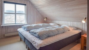 Une chambre avec un plafond en pente, une grande fenêtre, deux lampes de chevet et un lit recouvert d’une couette matelassée.