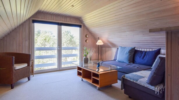 A cozy room with a sloped ceiling, a wicker sofa, a glass coffee table, and a large sliding glass door leading to an outdoor area. - Amazing home in Blåvand with sauna (Blåvand)