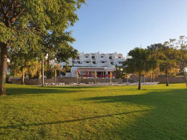A hotel with a white facade, outdoor seating area, and a well-maintained lawn.