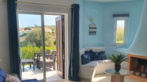 Una sala de estar con sofá, una silla, una mesita y vista al exterior.