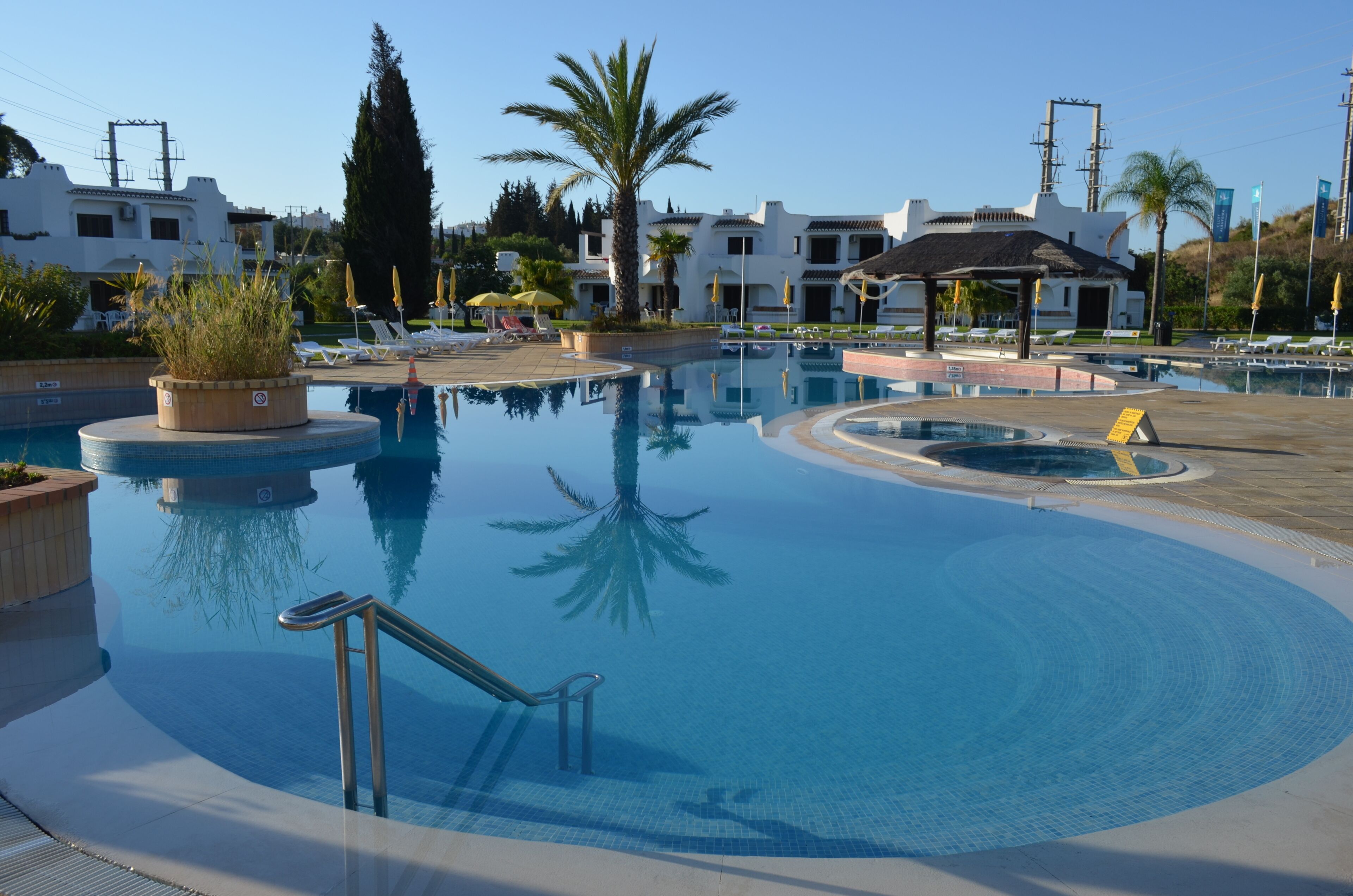Ein Pool mit kreisförmigem Design, umgeben von Liegestühlen und Sonnenschirmen, mit einem Gebäude im Hintergrund.