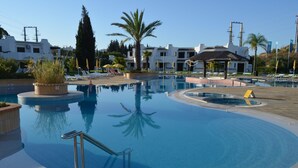 Una piscina de diseño circular, rodeada de sillones de descanso y sombrillas, con un edificio al fondo.