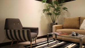 Una sala moderna con un sillón a rayas, un sofá, una mesa de centro de vidrio y una planta alta.