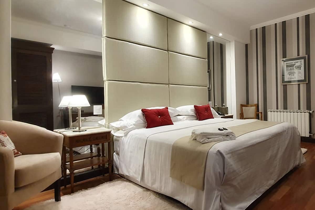 Ein Hotelzimmer mit einem großen Bett, einem Nachttisch mit Lampe, einem Sessel und einer Heizung.