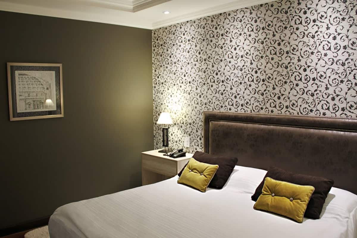Ein Hotelzimmer mit einem großen Bett, zwei Kissen, einem Nachttisch mit einer Lampe und einem gerahmten Bild an der Wand.