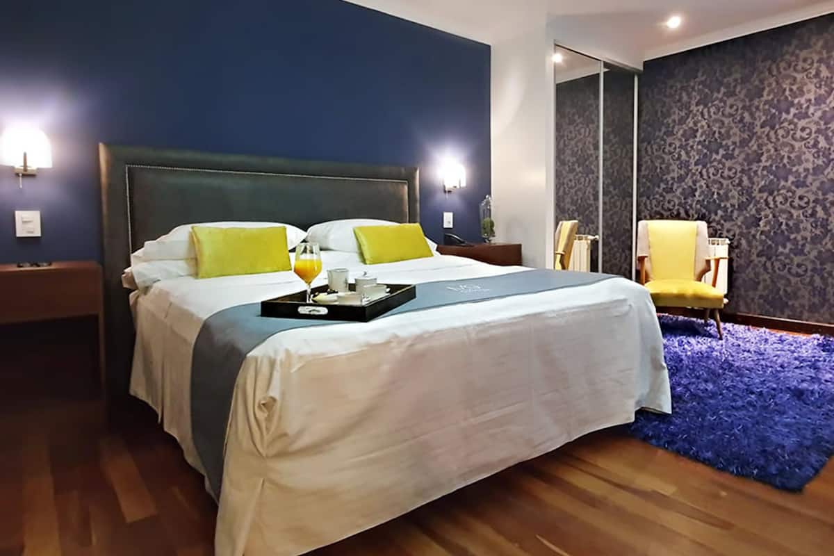 Ein Hotelzimmer mit einem großen Bett, einem Tablett mit Frühstücksgegenständen, einem Sessel und einem blauen Teppich.