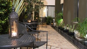 Un patio al aire libre con mesas y sillas de metal, un farol decorativo y plantas en macetas.